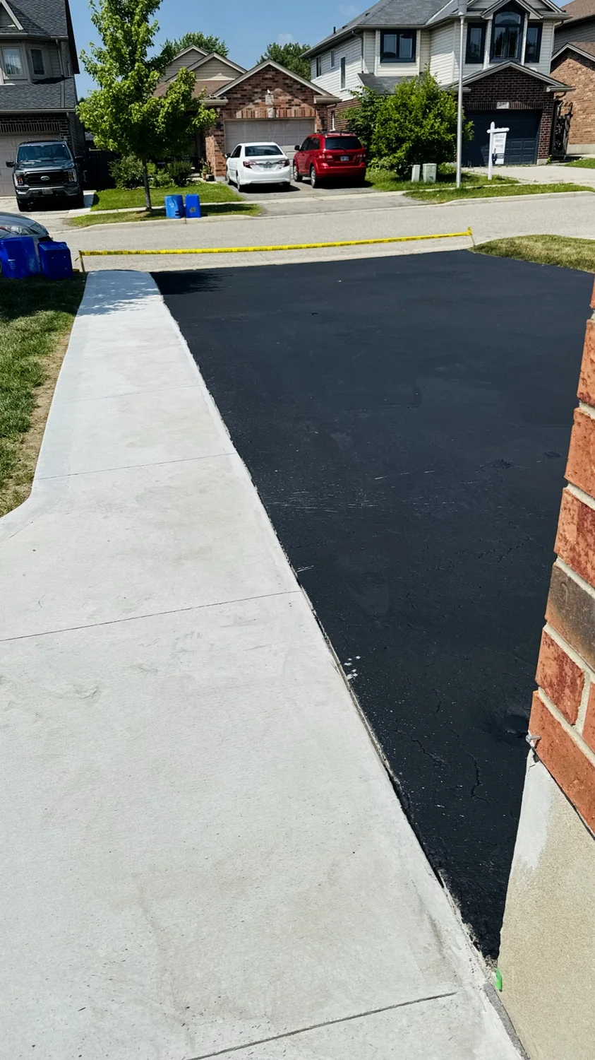 Clean asphalt driveway sealing edge beside a concrete walkway